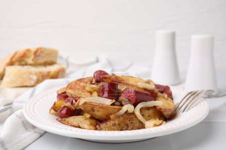 Köstliche Ofenkartoffeln mit dünnen, trockenen geräucherten Würstchen und Zwiebeln auf weißem Tisch, Nahaufnahme