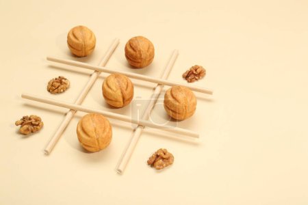 Tic tac toe game made with walnuts and cookies on beige background. Space for text