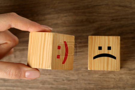 Photo for Woman choosing cube with happy face instead of another one with sad at wooden table, top view - Royalty Free Image