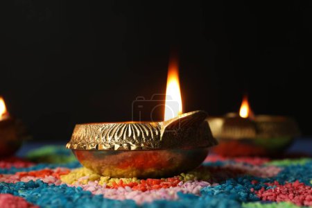 Téléchargez les photos : Fête de Diwali. Lampe Diya et rangoli coloré sur table sur fond noir, gros plan - en image libre de droit