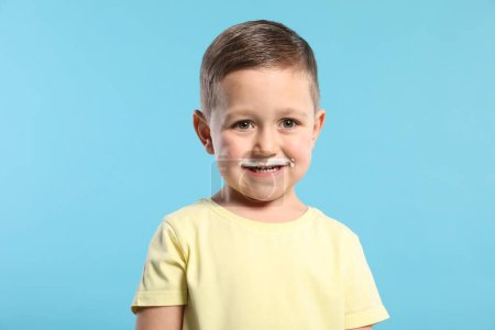 Téléchargez les photos : Mignon garçon avec moustache de lait sur fond bleu clair - en image libre de droit