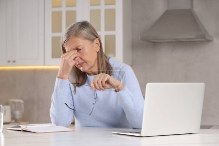 Menopausia. Mujer con gafas que sufren de dolor de cabeza en la mesa en la cocina