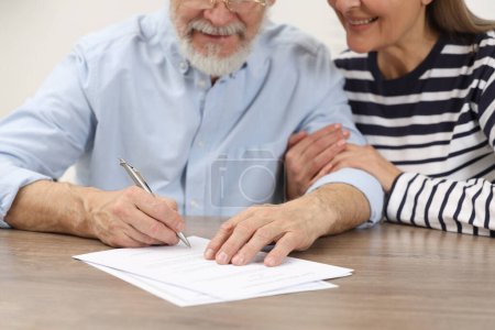 Foto de Feliz pareja de ancianos firmando Última Voluntad y Testamento en la mesa de madera, primer plano - Imagen libre de derechos