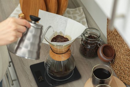 Téléchargez les photos : Femme versant de l'eau chaude dans une cafetière chemex en verre avec filtre en papier et café au comptoir dans la cuisine, vue ci-dessus - en image libre de droit
