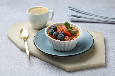 Foto de Deliciosa crema brulee con bayas y menta en un tazón servido en una mesa de textura gris - Imagen libre de derechos