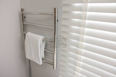Heated rail with towel on white wall in bathroom, space for text