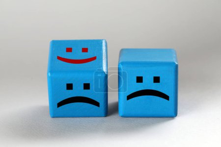 Cubos azules claros con caras tristes y felices sobre fondo gris claro
