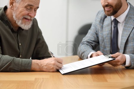 Foto de Notario sonriente que muestra al hombre mayor dónde firmar la última voluntad y el testamento en la mesa de madera en el interior, primer plano - Imagen libre de derechos