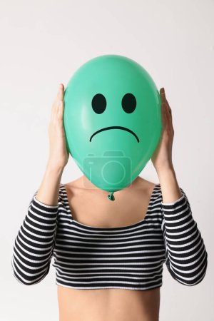 Frau versteckt sich hinter grünem Ballon mit traurigem Gesicht auf weißem Hintergrund