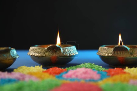 Diwali celebration. Diya lamps and colorful rangoli on table against black background, closeup
