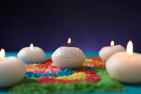 Diwali-Feier. Brennende Kerzen und bunte Rangoli vor violettem Hintergrund, Nahaufnahme