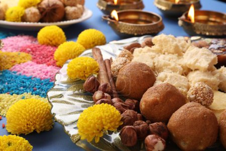 Diwali-Feier. Leckere indische Süßigkeiten, bunte Rangoli und Diya-Lampen auf blauem Tisch, Nahaufnahme
