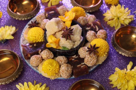 Diwali-Feier. Diya-Lampen, leckere indische Süßigkeiten und gelbe Blumen auf einem violetten Tisch