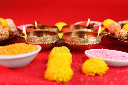 Diwali-Feier. Diya-Lampen und leuchtende Rangoli auf leuchtend rotem Tisch, Nahaufnahme