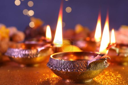 Diwali celebration. Diya lamps on shiny golden table against blurred lights, closeup