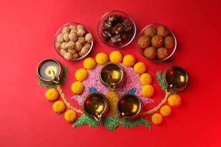 Glücklicher Diwali. Flache Komposition mit Diya-Lampen, bunten Rangoli und indischen Süßigkeiten auf rotem Tisch