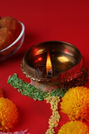 Glücklicher Diwali. Diya-Lampe, bunte Rangoli und Blumen auf rotem Tisch, Nahaufnahme