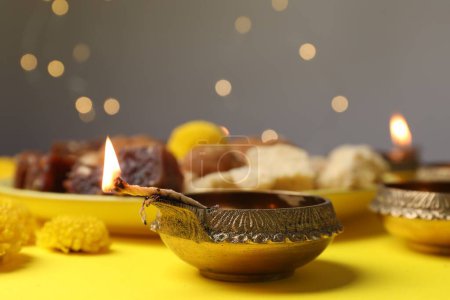 Happy Diwali. Diya lamp on yellow table against blurred lights, closeup
