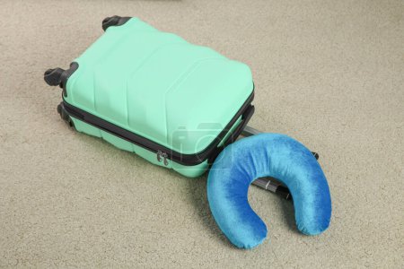 Light blue travel pillow and suitcase on beige rug
