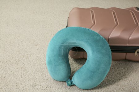 Turquoise travel pillow and suitcase on beige rug, space for text