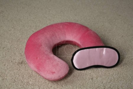 Pink travel pillow and sleep mask on beige rug