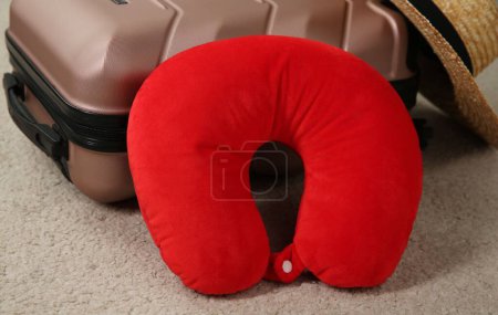 Red travel pillow and suitcase on beige rug, closeup