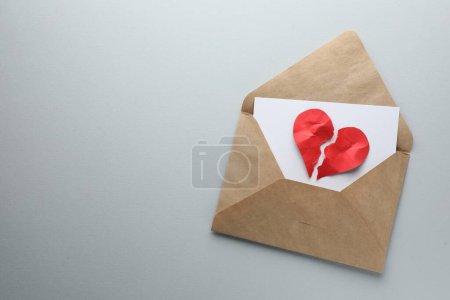 Coeur brisé. Enveloppe avec des moitiés de coeur en papier rouge déchiré sur fond blanc, vue de dessus. Espace pour le texte