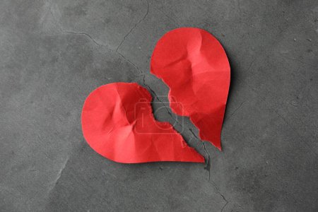 Moitiés de coeur en papier rouge déchiré sur table grise, vue de dessus. Coeur brisé
