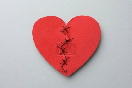 Coeur brisé. Coeur en papier rouge déchiré cousu avec fil sur fond gris clair, vue de dessus