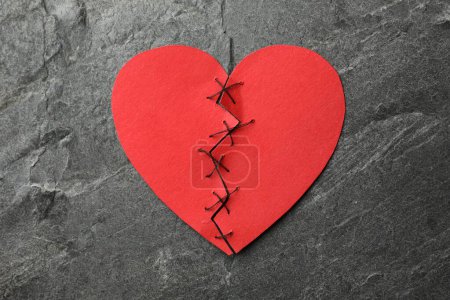 Coeur brisé. Coeur en papier rouge déchiré cousu avec fil sur table gris foncé, vue de dessus