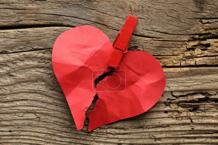Coeur brisé. Coeur en papier rouge déchiré avec une pince à linge sur une table en bois, vue de dessus