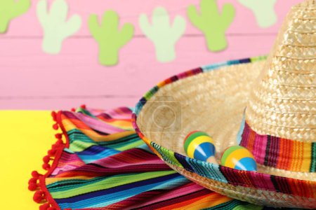 Chapeau sombrero mexicain, poncho et maracas sur table jaune, gros plan. Espace pour le texte