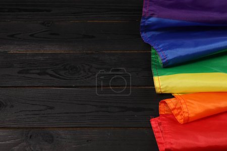 Rainbow LGBT flag on black wooden background, top view. Space for text