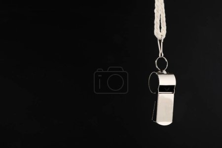 Referee equipment. Metal whistle on black background, closeup and space for text