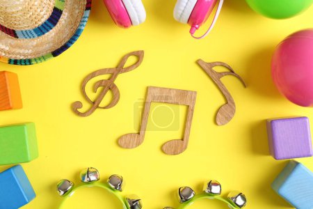 Photo for Baby song concept. Wooden notes, tambourines and toys on yellow background, flat lay - Royalty Free Image