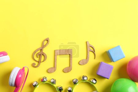 Concepto de canción de bebé. Notas de madera, panderetas y juguetes sobre fondo amarillo, plano. Espacio para texto