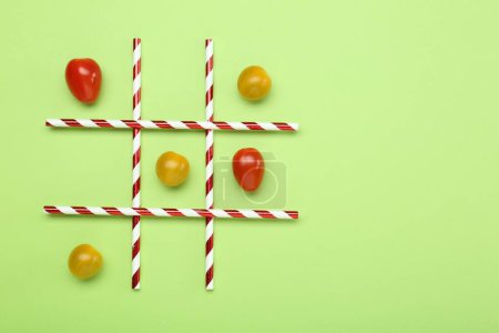 Tic tac toe game made with cherry tomatoes on light green background, top view
