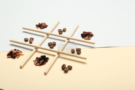 Tic tac toe game made with coffee beans and dry tea leaves on color background