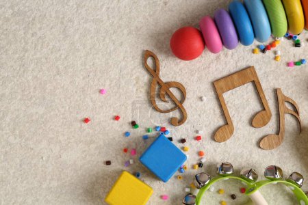 Baby song concept. Wooden notes, kids musical instruments and toys on beige carpet, flat lay. Space for text