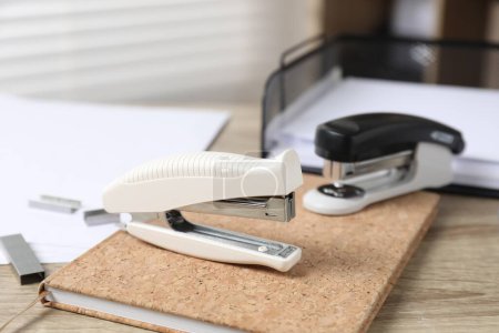 Staplers and notebook on wooden table indoors, closeup