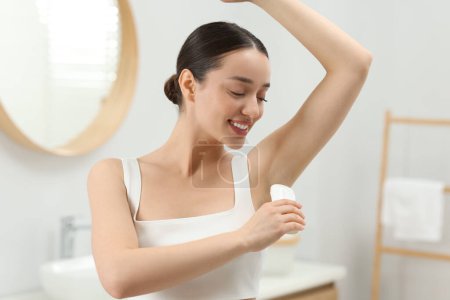Hermosa mujer joven aplicando desodorante en el baño
