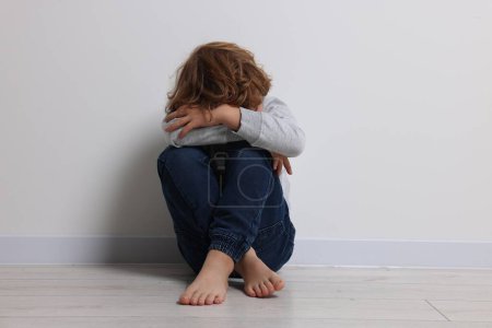 Child abuse. Upset boy sitting on floor near white wall