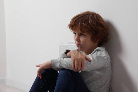 Kindesmissbrauch. Aufgebrachter Junge sitzt auf dem Boden neben weißer Wand