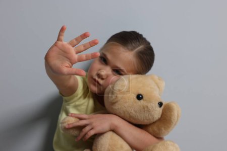 Kindesmissbrauch. Mädchen mit Spielzeug macht Stop-Geste in der Nähe der grauen Wand, selektiver Fokus