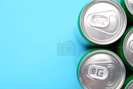 Bebida energética en latas sobre fondo azul claro, vista superior. Espacio para texto