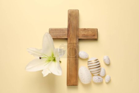 Photo for Wooden cross, painted Easter eggs and lily flower on pale yellow background, flat lay - Royalty Free Image
