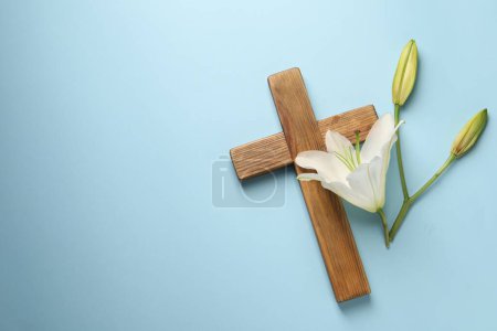 Photo for Wooden cross and lily flowers on light blue background, top view with space for text. Easter attributes - Royalty Free Image