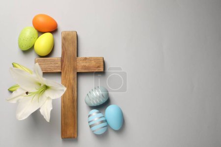 Photo for Wooden cross, painted Easter eggs and lily flowers on grey background, flat lay. Space for text - Royalty Free Image