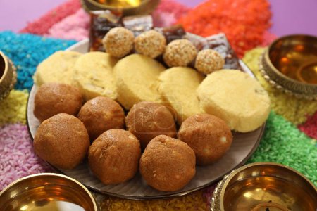 Diwali-Feier. Leckere indische Süßigkeiten, Diya-Lampen und bunte Rangoli auf dem Tisch, Nahaufnahme