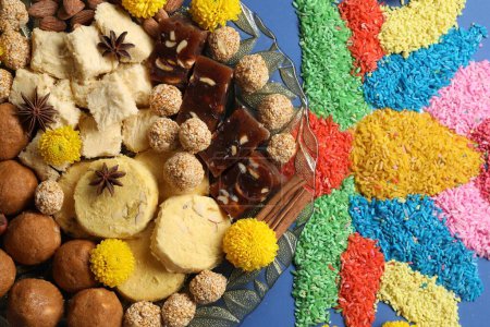 Diwali celebration. Tasty Indian sweets, spices, nuts and colorful rangoli on blue table, flat lay